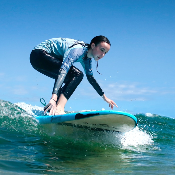 Niña cogiendo una ola durante el surf camp 24/7 en la Playa de Loredo - Somo, aprendiendo a surfear en Cantabria